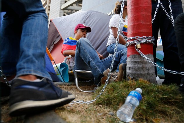 Anti-government protesters sit chained at a protest as they camp in front of UN offices in Caracas