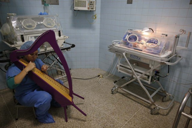 A member of "El Sistema" plays on a harp, as part of its "New Members" program, next to a newborn baby at a public maternity hospital in Caracas