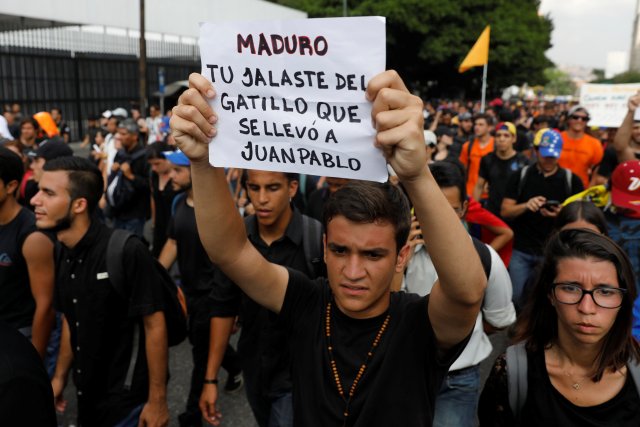 A student holding a sign that reads, "Maduro, you pulled the trigger that took to Juan Pablo", takes part in a tribute to Juan Pablo Pernalete, who died after being hit by a tear gas shot during a protest against Venezuelan President Nicolas Maduro, in Caracas, Venezuela April 27, 2017. REUTERS/Carlos Garcia Rawlins
