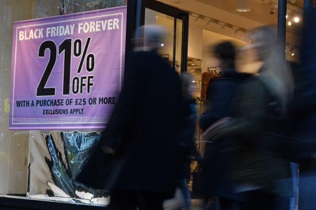 Shoppers pass a promotional sign for 'Black Friday' sales discounts on Oxford Street in London, on November 23, 2017. Black Friday is a sales offer originating from the US where retailers slash prices on the day after the Thanksgiving holiday. In the UK it is used as a marketing device to entice Christmas shoppers with the discounts at stores often lasting for a week. / AFP PHOTO / Ben STANSALL