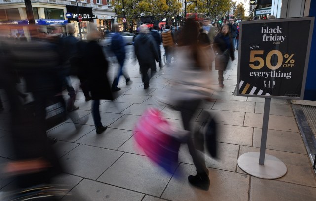 Shoppers pass a promotional sign for 'Black Friday' sales discounts as they exit a retail store on Oxford Street in London, on November 23, 2017. Black Friday is a sales offer originating from the US where retailers slash prices on the day after the Thanksgiving holiday. In the UK it is used as a marketing device to entice Christmas shoppers with the discounts at stores often lasting for a week. / AFP PHOTO / Ben STANSALL