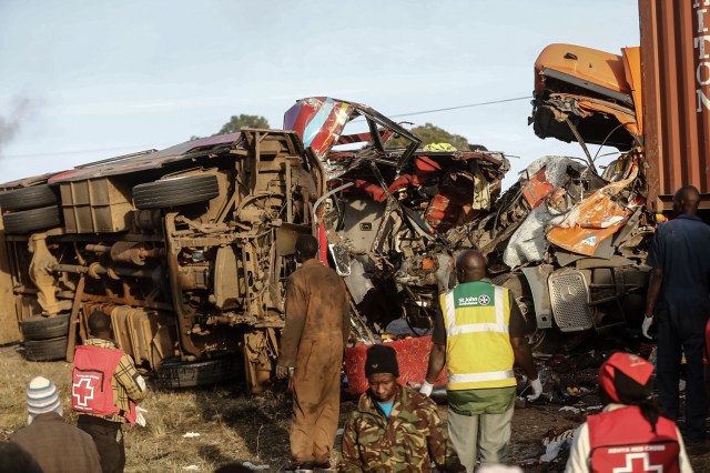 Emergency workers stand near the wreckage of a bus and a lorry that crashed in a head-on collision, killing thirty people, at the accident scene near Nakuru, Kenya, on December 31, 2017. Thirty people were killed and 16 injured early on the morning of December 31 in a head-on collision between a bus and a lorry on a road in central Kenya, police said. The accident occurred close to a notorious stretch on the Nakuru-Eldoret highway when a bus travelling from Busia, in western Kenya, collided with a truck coming from Nakuru. Police said the death toll for that stretch of road has now reached 100 this month alone. / AFP PHOTO / STR