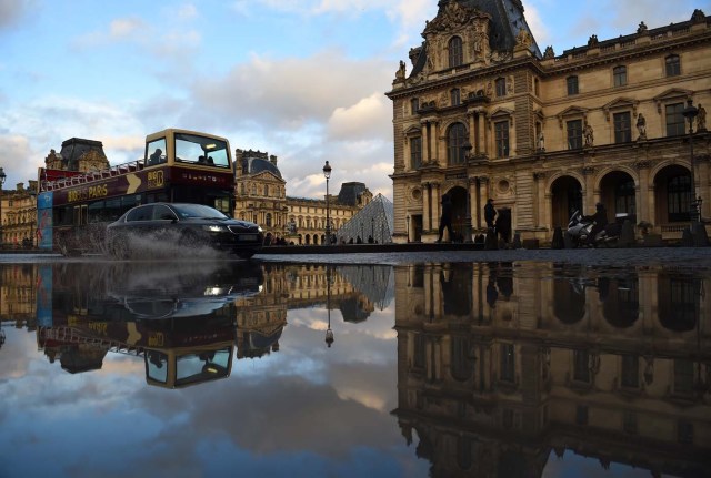 A car overtakes a double decker sightseeing bus past the Louvre Museum, reflected in a pool of rain water on January 1, 2018 in Paris. / AFP PHOTO / GUILLAUME SOUVANT